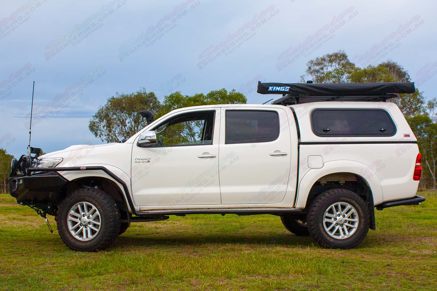 Left side view of a white dual cab Toyota Hilux fitted with a 2 inch Bilstein Suspension kit, Superior upper control arms and swaybar relocation plate