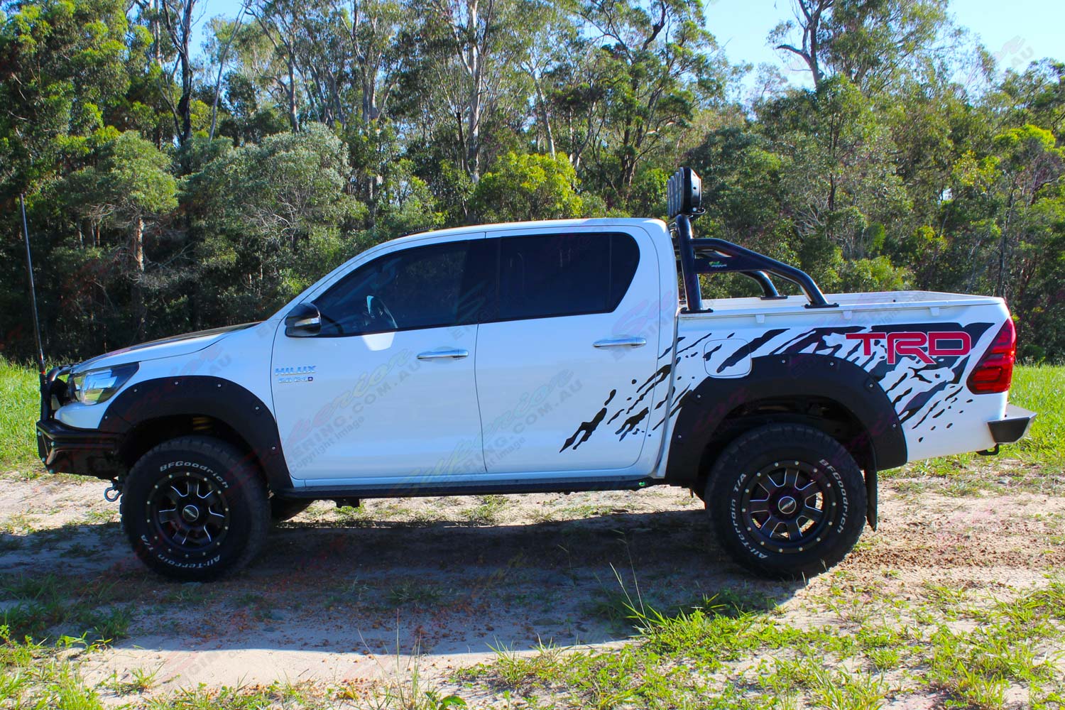 Left side view of a white Toyota Hilux Revo (dual cab) fitted with Australian made Lightforce HTX Hybrid HID LEDs and Ironman 4x4 side steps, sportsbar, flood lights and rear protection bar - by Superior Engineering
