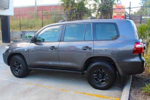 Left side view of a dark grey 200 Series Toyota Landcruiser 4wd fitted with a set of heavy duty Superior Engineering stealth rock sliders