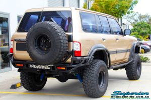 Rear right view of a Gold Nissan GU Patrol Wagon being fitted with Superior Lower Control Arms, Adjustable Upper Control Arms, Comp Spec 4340m Drag Link, 4" Inch Front & Rear Dobinson Coil Springs, Superior Coil Tower Brace and Superior 5" Inch Remote Reservoir Front & Rear Shocks