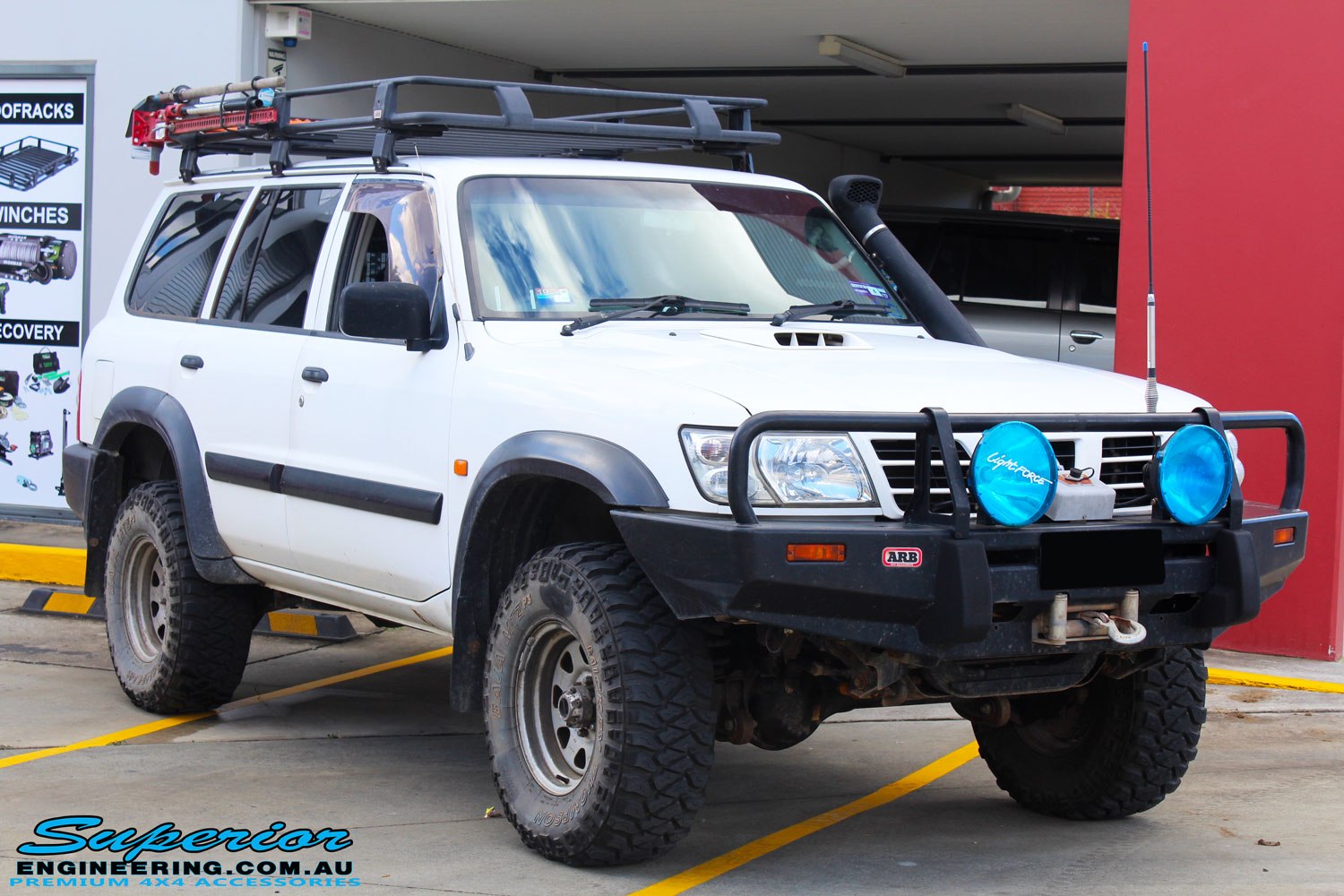 Right front side view of a Nissan GU Patrol Wagon in White On The Hoist @ Superior Engineering Deception Bay Showroom