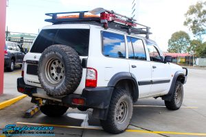 Rear left view of a Nissan GU Patrol Wagon in White On The Hoist @ Superior Engineering Deception Bay Showroom