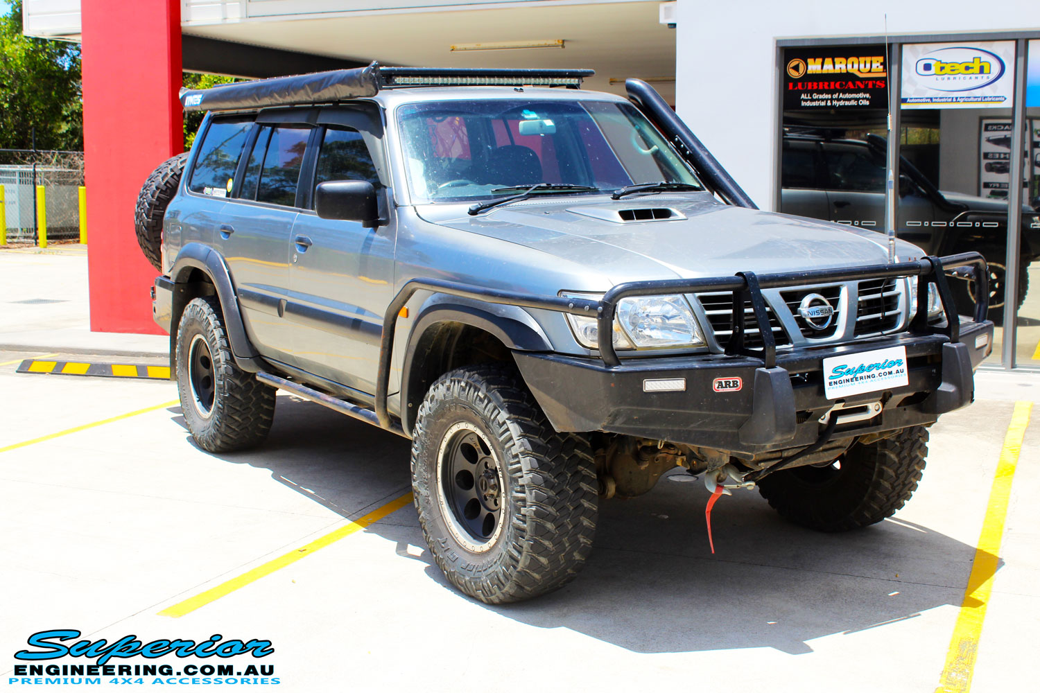 Right front side view of a Nissan GU Patrol Wagon in Silver On The Hoist @ Superior Engineering Deception Bay Showroom getting fitted with a Superior Coil Tower Brace Kit