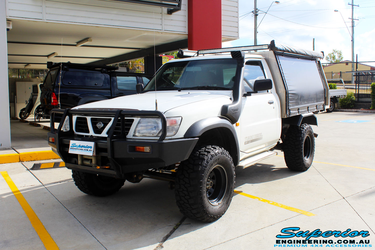 Left front side view of a Nissan GU Patrol Ute in White On The Hoist @ Superior Engineering Deception Bay Showroom