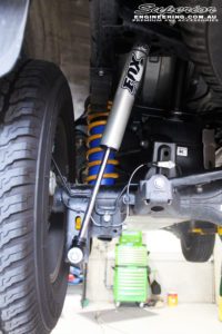 Rear left underbody view of the fitted Rear Fox 2.0 Performance Series IFP Shock, Coil Spring, Airbag Man Coil Helper Air Kit with U-Bolt Kit and Shackles